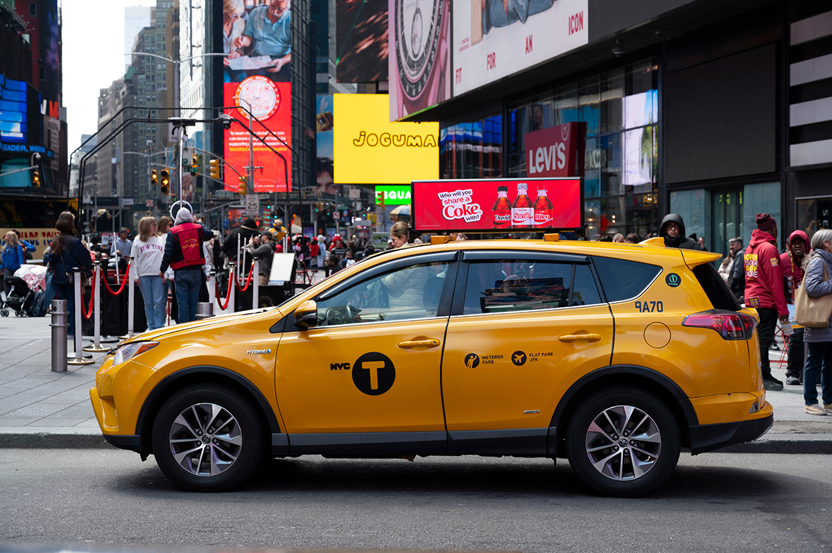 NYC yellow taxi with digital LED advertising display on top driving through Times Square